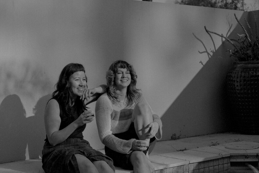 Two woman sit near a pool 