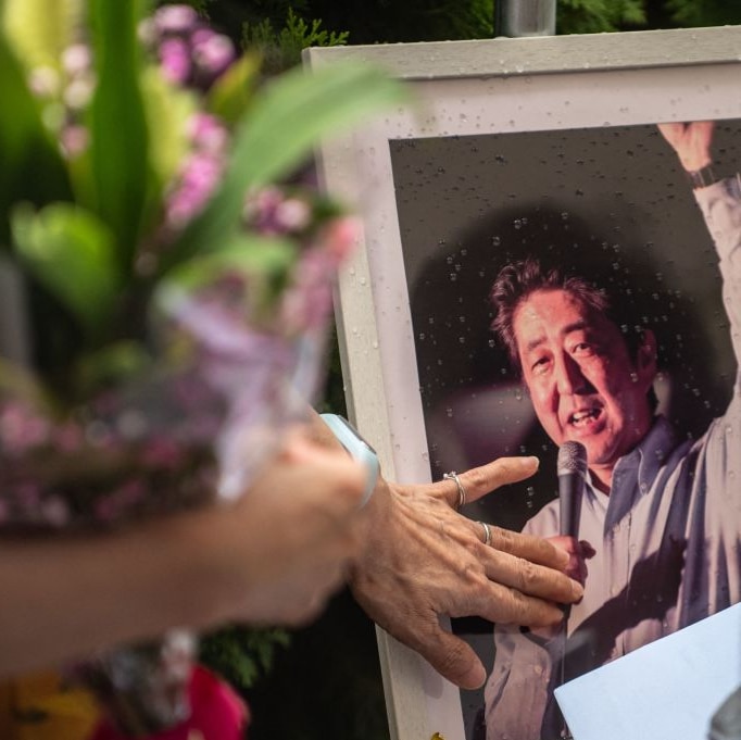 A blurred image of a woman with flowers and a large  photo of Shinzo Abe at a makeshift shrine