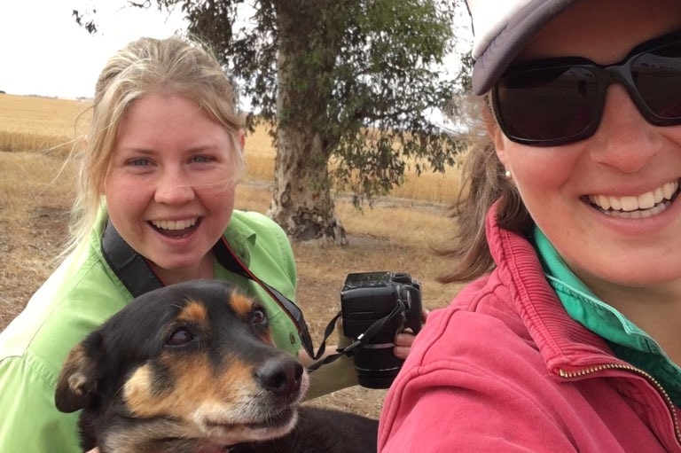 two girls smile on a farm with a dog