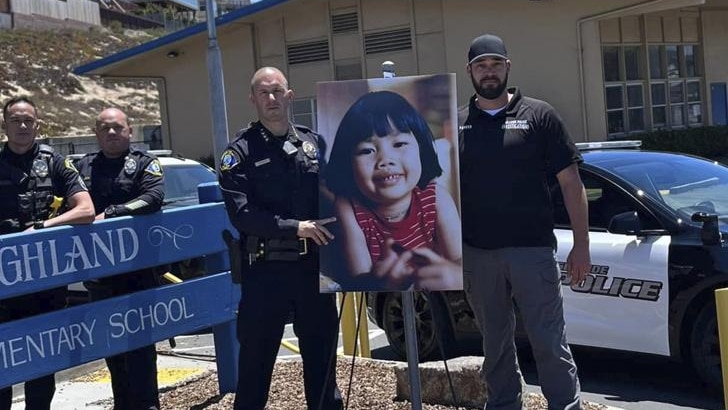 Police officers stand beside a sign that reads Highland Elementary School and a poster of a young girl with short black hair sm