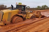 A grader bogged in the red dirt road.