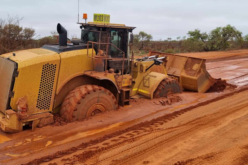 A grader bogged in the red dirt road.