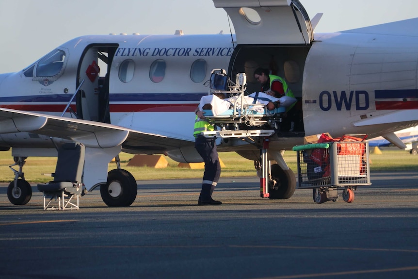 Two paramedics unload a stretcher holding a patient from an RFDS aircraft.