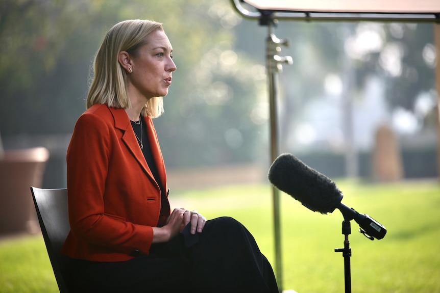 A side-on shot of Mia Davies sitting down talking in front of a microphone during an interview outdoors.