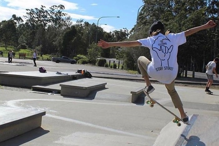 A boy in a white shirt and black hat jumps a skateboard off a ramp.