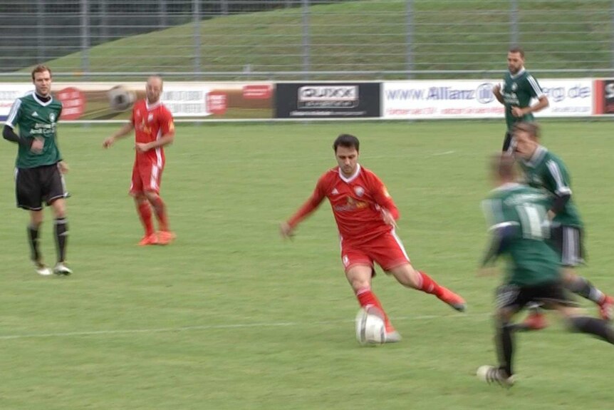 A man wearing a red uniform kicks a soccerball on field.