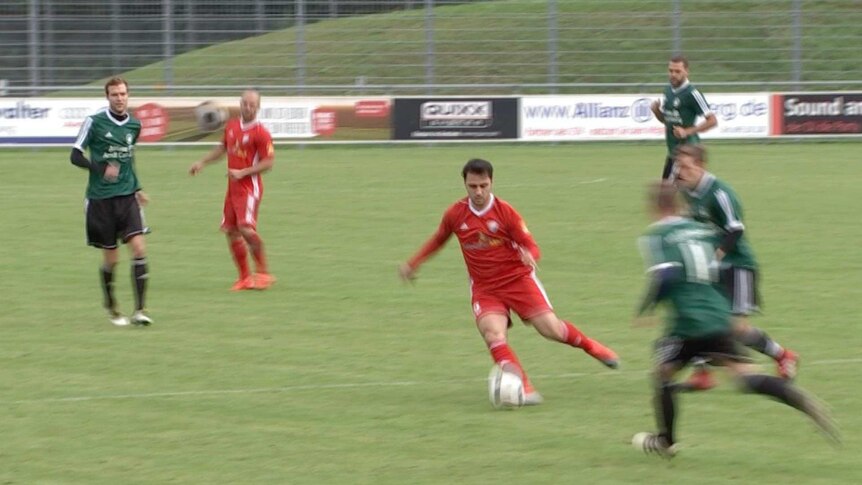 A man wearing a red uniform kicks a soccerball on field.
