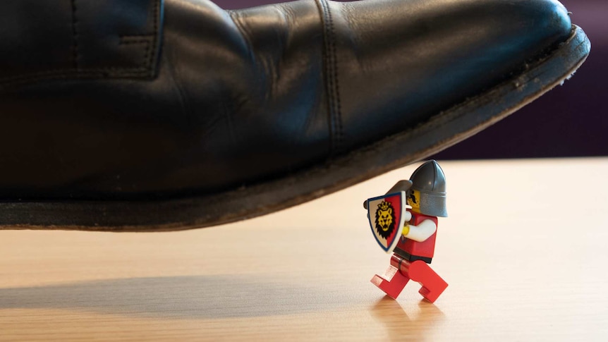 A Lego figure dressed as a knight is squashed by a man's leather shoe.