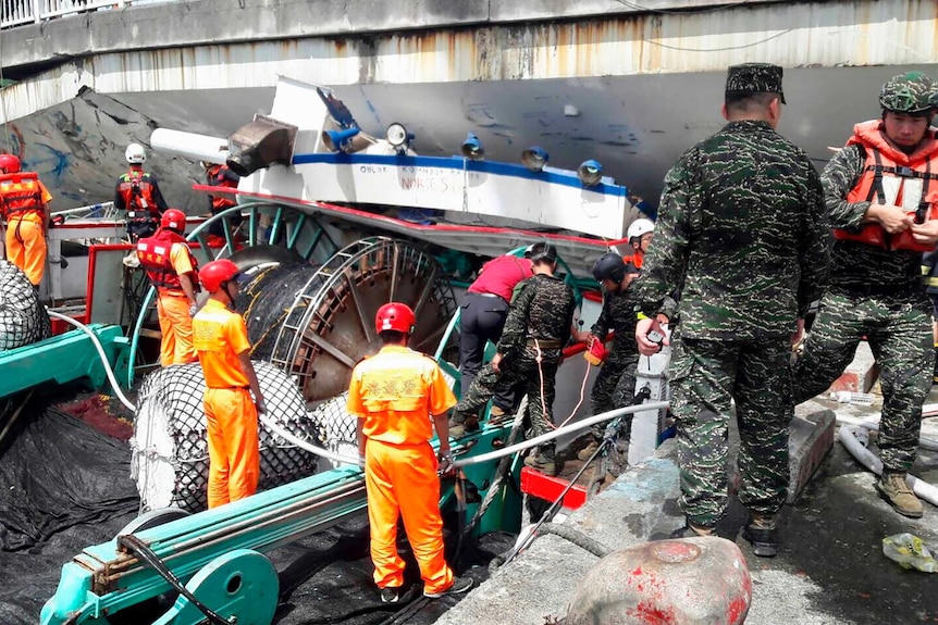 At least 10 people are seen among the wreckage of a bridge with shipping materials seen underneath it. It is daytime.