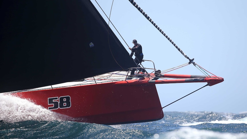 A sailor stands near the front of a red yacht with the number 58 painted on it.