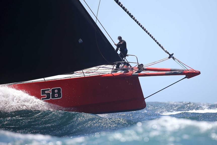 A sailor stands near the front of a red yacht with the number 58 painted on it.