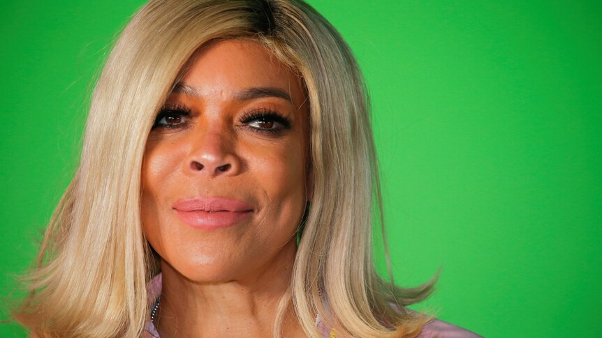 A close up headshot of Wendy Williams with blonde hair against a green background