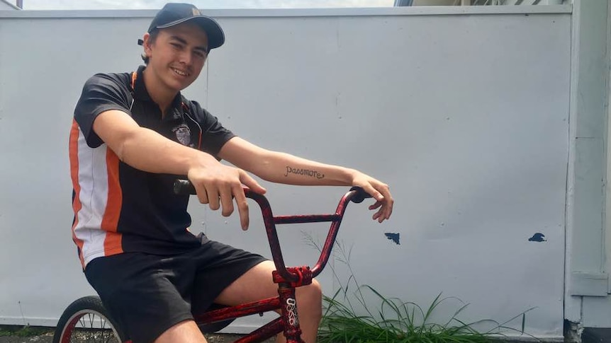 Teenage boy sits on a broken BMX bike