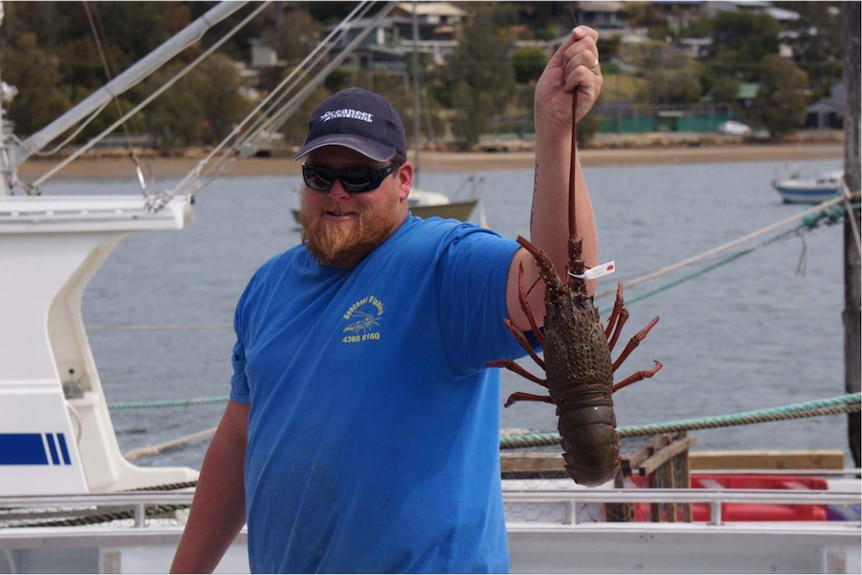 Fisherman holding up a lobster on a fishing boat