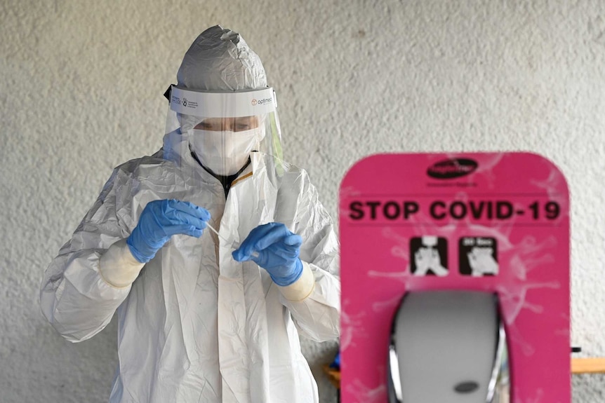 a person in protective equipment holds up a sample next to a sign that reads stop covid-19
