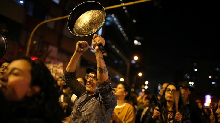 A man is seen with a frying pan in one hand and a wooden spoon in the other. He is the focus of an image of protesters.