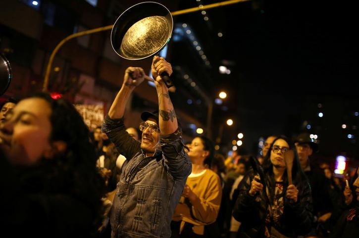 A man is seen with a frying pan in one hand and a wooden spoon in the other. He is the focus of an image of protesters.