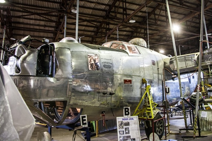 A large, silver antique aeroplane sits inside a hangar.