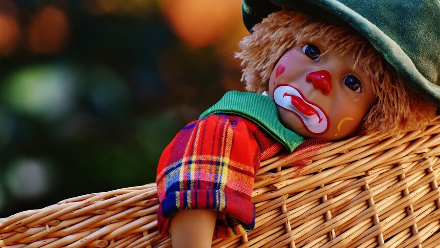 Photo of doll with a sad clown face in a woven basket