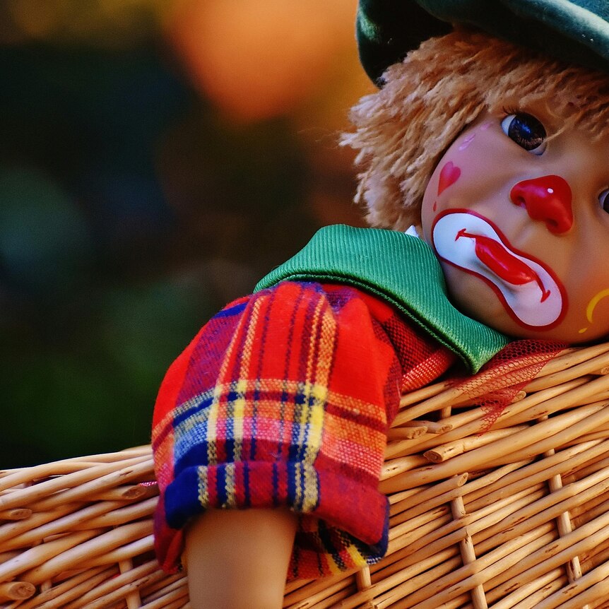 Photo of doll with a sad clown face in a woven basket