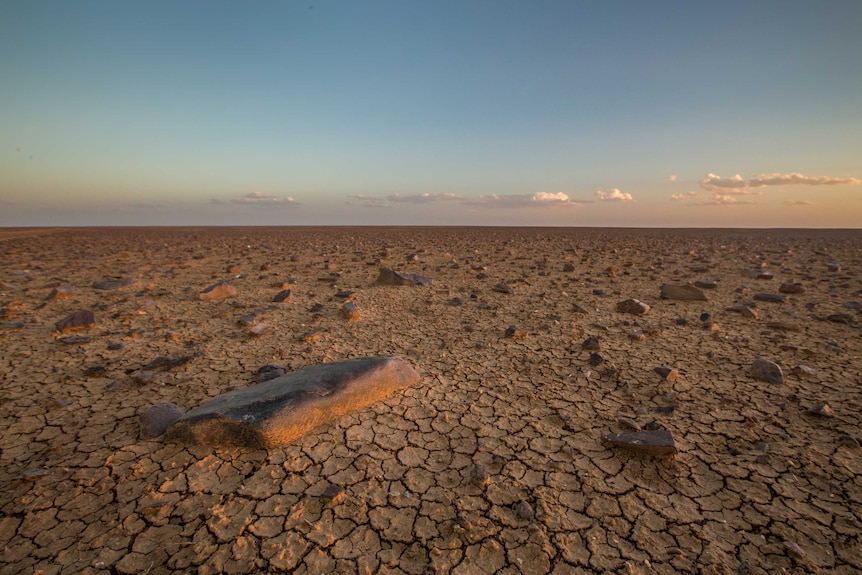 A moon-like landscape stretches out, with small rocks dotted off into the distance against a fading blue sky.