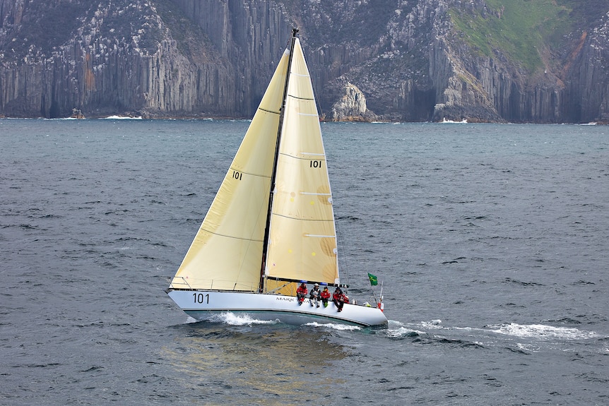 An old yacht sailing with cliffs behind.