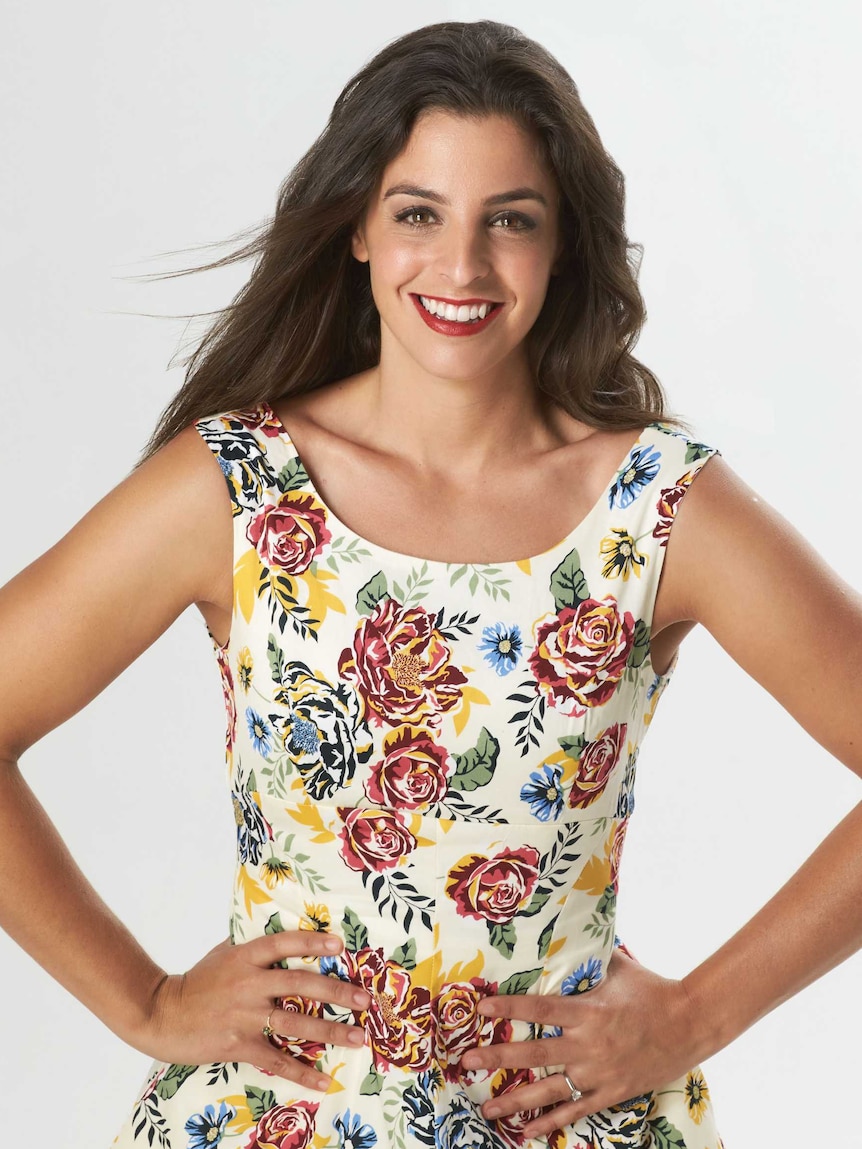 A pretty young woman in a floral dress smiles at the camera.