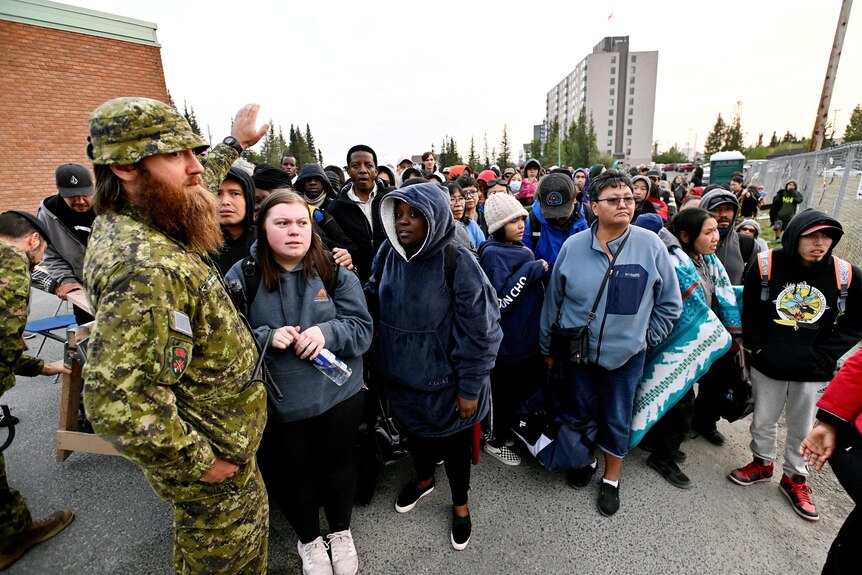 A crowd lines up behind a soldier with his hand up 
