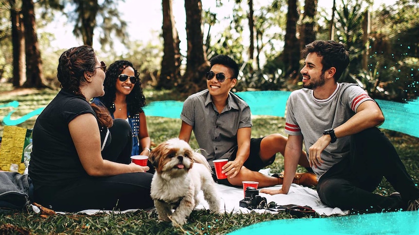 Group of young students and a dog sitting on grass, smiling while holding red plastic cups for a story about making uni friends.