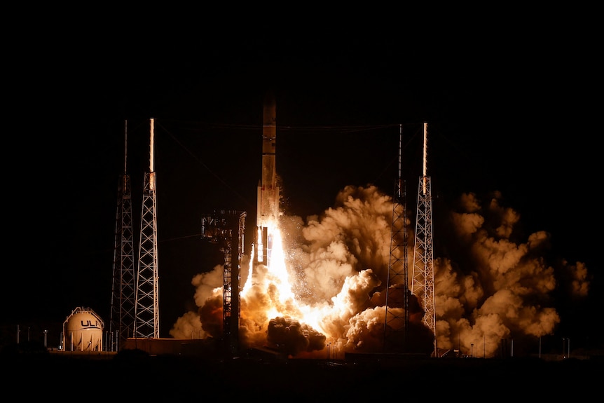 A large white rocket blasts off a launchpad in a cloud of smoke and flames at night.