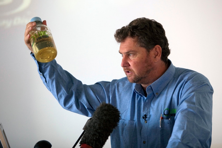 A man in a business shirt and tie gestures while he speaks to an unseen crowd.