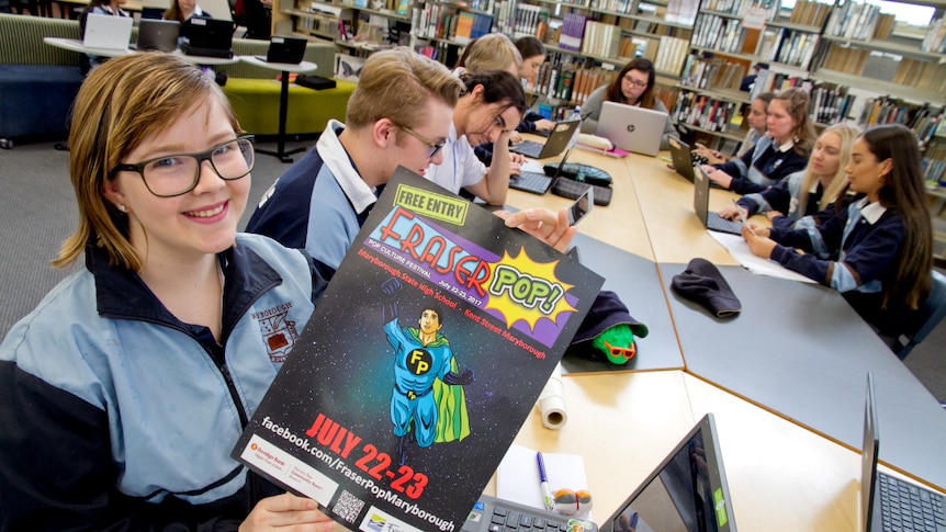 A teenage girl with glasses holds a poster for the pop culture festival, Fraserpop.