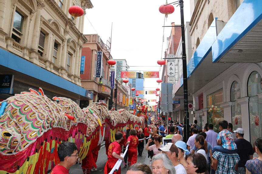 A dragon dances through a crowd of people in a street in Chinatown.