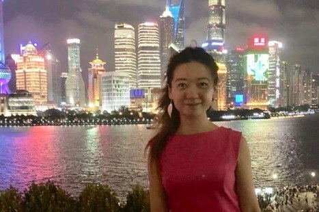 Woman smiles at camera standing in front of night skyline of city.