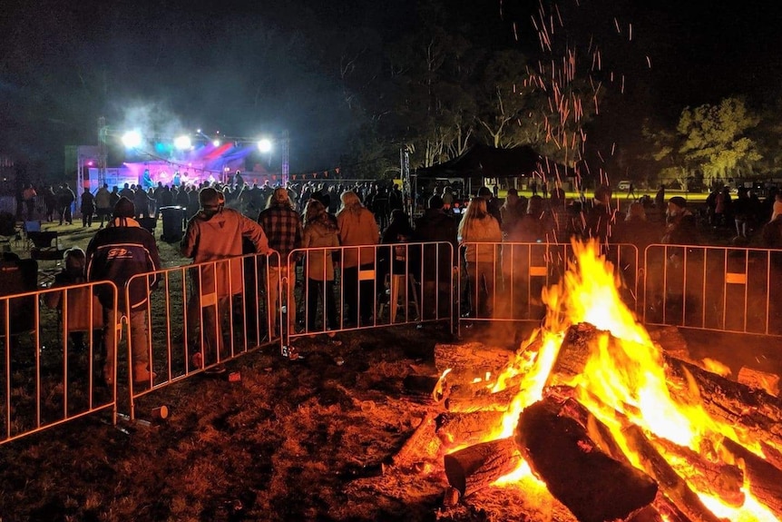 A group of people have their backs to a large bonfire while a live band plays in the background.
