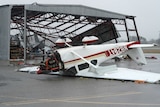 A plane lies upside down outside a damaged hangar at an airport