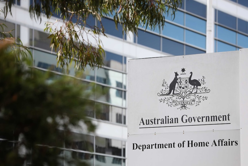 A sign saying "Australian Government Department of Home Affairs" outside a tall building. There are leaves in the foreground