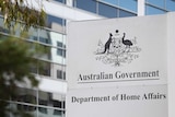 A sign saying "Australian Government Department of Home Affairs" outside a tall building. There are leaves in the foreground