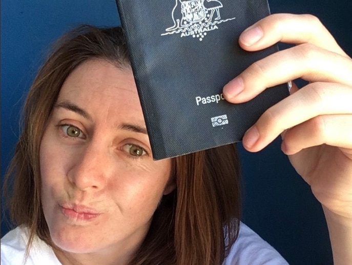 A woman with brown hair holding up her Australian passport