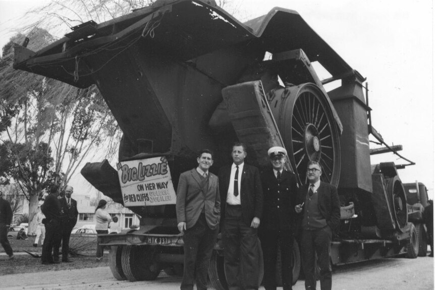 Black and white photo of giant tractor with men standing beside the wheel