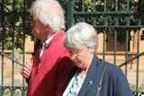 A man and a woman hold hands as they walk in front of an ornate fence.