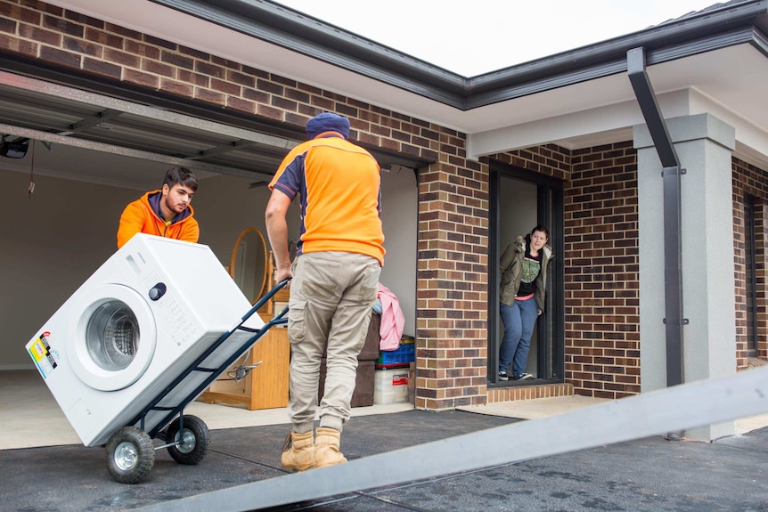 Nicki Ellis watches the removalists move the washing machine into her new home.