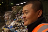 Nathan Ung, wearing an orange high-visibility vest, at a recycling plant. Rubbish is visible behind him.