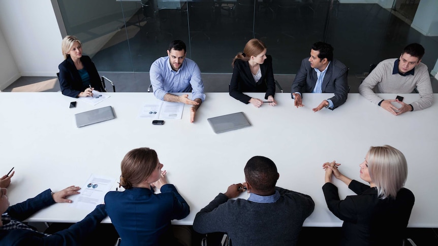 Aerial shot of nine business people sitting around a desk in a board room.