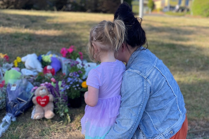 A little girl leans against her mother as they look at the flowers and soft toys left for the children.