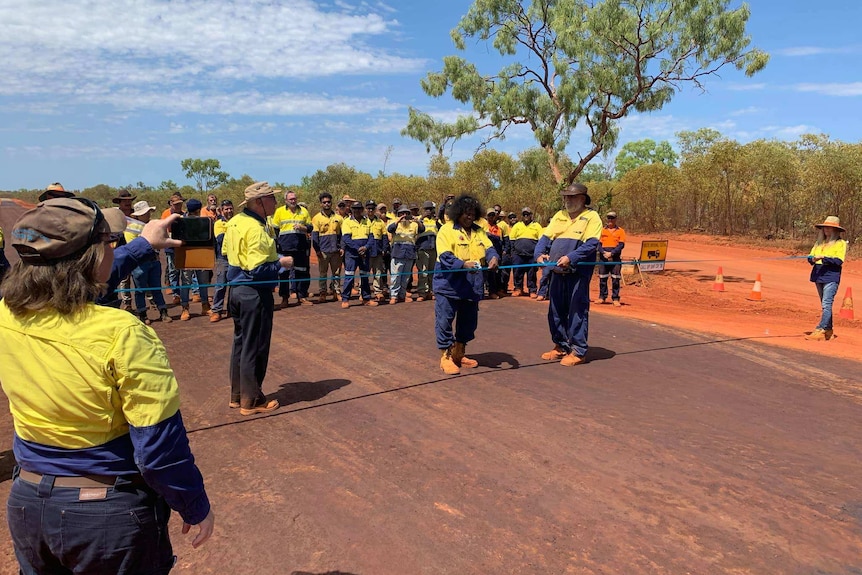 A group of workers on the finished Cape Leveque Road, with a man in hi-vis cutting the ribbon.