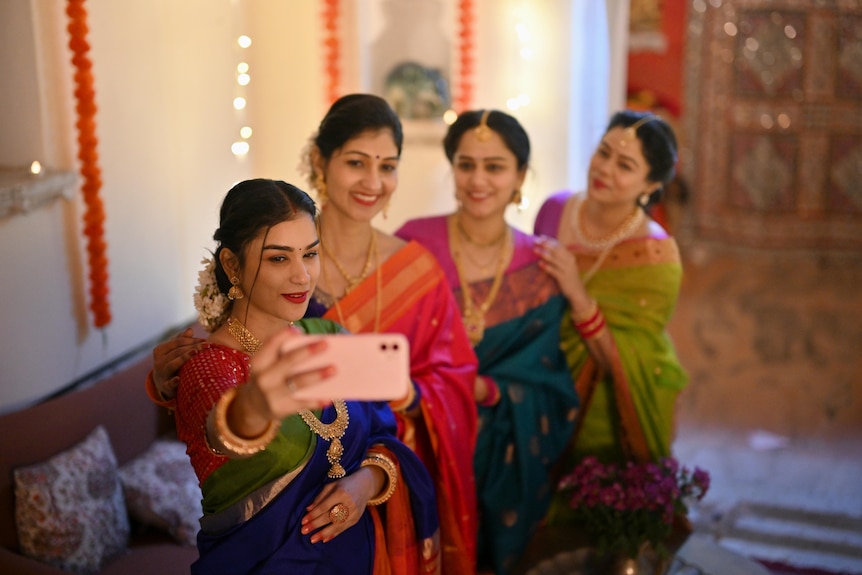 Four people in colourful traditional outfits standing in line, smiling and laughing.