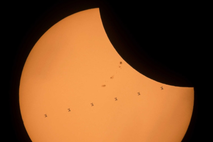 A composite image shows the International Space Station passing in front, as the Moon eclipses one side of the Sun.
