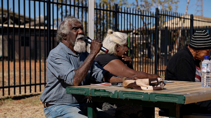 Eddie Robertson speaks into a microphone sitting at a table in Yuendumu.