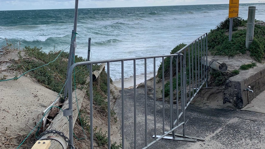 A barrier across a beach path amid stormy skies.